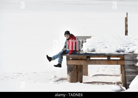 Austria, Tirolo, Achensee, donna seduta sul molo in inverno Foto Stock