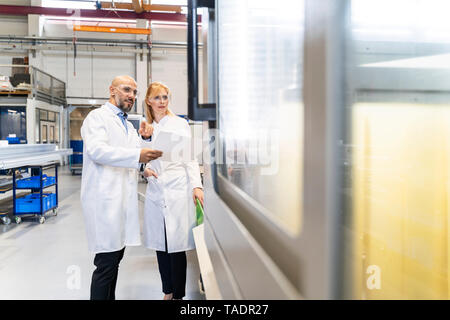 Due tecnici indossano camici da laboratorio e occhiali di sicurezza esaminando la macchina Foto Stock