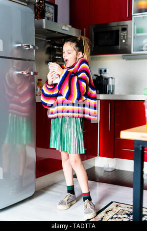 Ragazza eccitato in striped pullover in cucina a casa mangiare il cioccolato Foto Stock