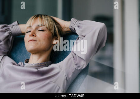 Donna bionda rilassante in poltrona, con le mani dietro la testa Foto Stock