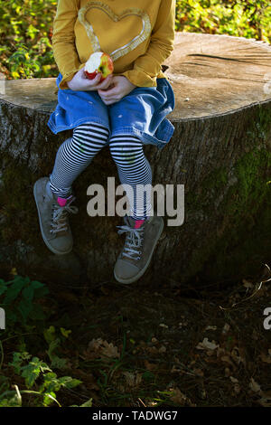 Sezione bassa della ragazza con un Apple seduto su un ceppo di albero Foto Stock
