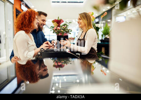 Coppia felice e shop assistant con pianta in vaso a contatore nel negozio di fiori Foto Stock