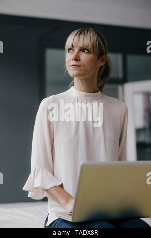 Donna seduta sul lettino, utilizzando laptop Foto Stock