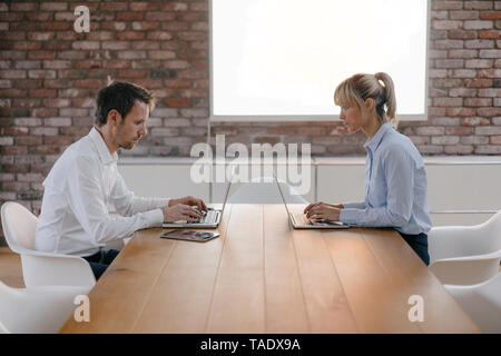 Imprenditore e donna seduta alla scrivania, lavorando sul computer portatile Foto Stock