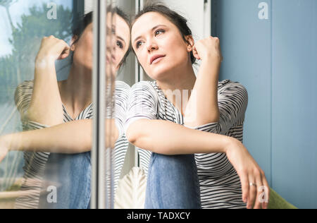 Grave donna guardando fuori della finestra a casa Foto Stock