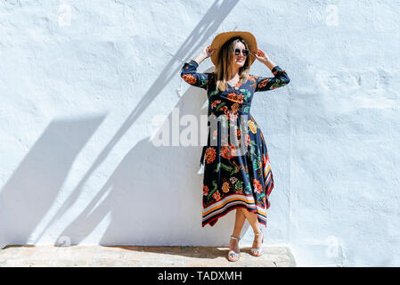 Spagna, Cadiz, Vejer de la Frontera, moda donna con cappello di paglia in piedi di fronte a muro bianco Foto Stock