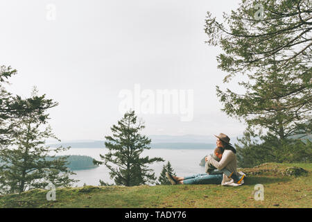 Madre seduta su erba, coccole a suo figlio nella Natura Foto Stock