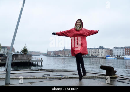 Danimarca, Copenaghen, donna felice jumping al waterfront in condizioni di tempo piovoso Foto Stock