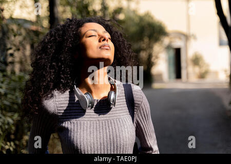 Ritratto di una donna con le cuffie, godersi il sole con gli occhi chiusi Foto Stock