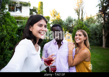 Amici divertendosi ad una cena estiva in giardino, tenendo selfies Foto Stock