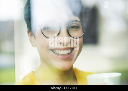 Ritratto di donna ridere con tazza di caffè dietro il vetro di finestra Foto Stock