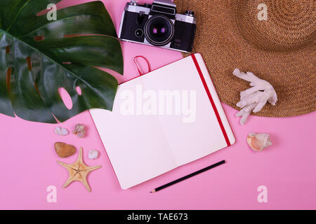 Donna Accessori viaggiatori: corallo, shell, stelle marine, cappello di paglia, foglia tropicale monstera, fotocamera retrò, notebook con copia spazio, penna su backgroun rosa Foto Stock