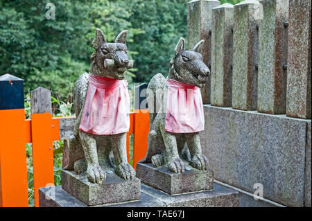 Due kitsune o messenger fox statue, indossando red bibs, presso Lo Shinto Fushimi Inari santuario nel sud di Kyoto, Giappone. Foto Stock