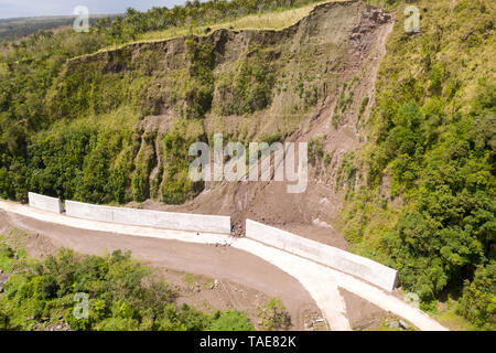 Strada con recinzioni in cemento sull'isola di Camiguin, Filippine. Protezione della strada da frane e frane. Il crollo del suolo sulla strada nelle alture. Foto Stock