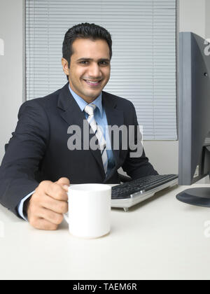 CORPORATE EXECUTIVE bere il tè/caffè mentre si lavora alla propria scrivania Foto Stock