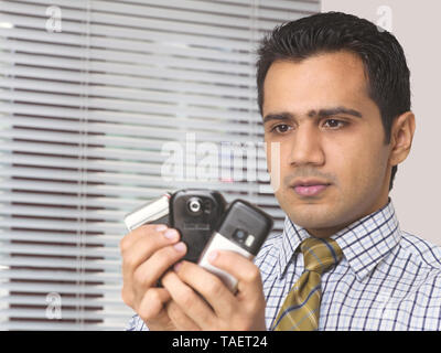 Uomo in possesso di più telefoni cellulari nelle sue mani Foto Stock