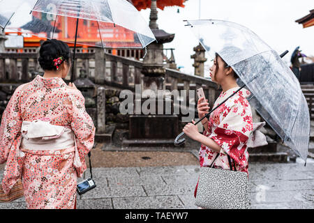 Kyoto, Giappone - Aprile 9, 2019: due donne con kimono e ombrelloni in piedi durante il giorno di pioggia a Kiyomizu-dera tempio Foto Stock