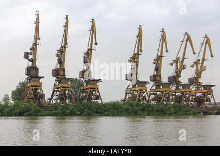 Più vecchio arrugginito Gantry cranes stand in fila su una ricoperta in riva al fiume Foto Stock