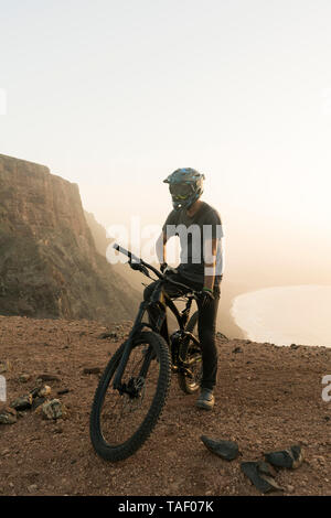 Spagna, Lanzarote, mountainbiker su un viaggio lungo la costa al tramonto Foto Stock