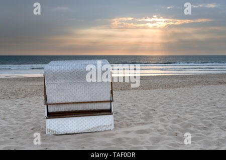 Germania Sylt, Mare del Nord, la spiaggia di sabbia con cappuccio sedia spiaggia in sunset Foto Stock