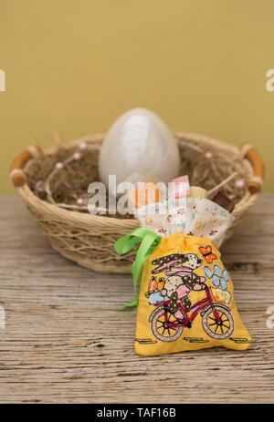 Un sacchetto con doni ha un grazioso ricamo. Una bici coniglietto di pasqua è stato applicato. Dietro il sacco è una copia dello spazio e un nido di Pasqua con uovo. Foto Stock