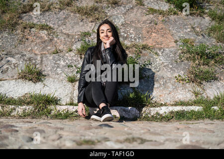 Ritratto di giovane sorridente donna seduta sul marciapiede Foto Stock