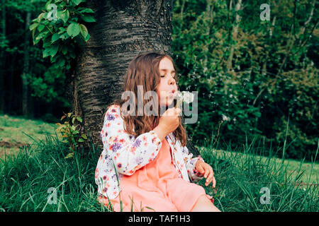 Ritratto di ragazza seduta su un prato blowball soffiaggio Foto Stock