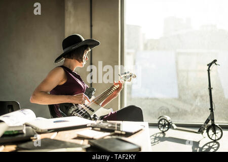 Donna con cappello seduto in ufficio, suonare la chitarra ha Foto Stock