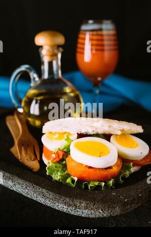 Arepa con uovo e verdure per la colazione, servita su una pietra vulcanica di piastra con un bicchiere di succo di papaia Foto Stock