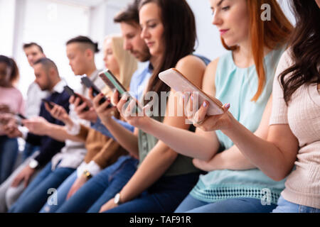 Multi-etnico Giovani appoggiata vicino a tavola in fila utilizza lo smartphone Foto Stock