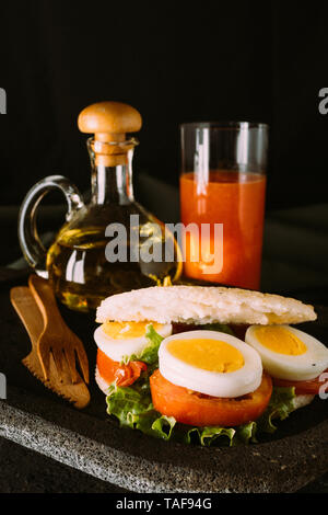 Arepa con uovo e verdure per la colazione, servita su una pietra vulcanica di piastra con un bicchiere di succo di papaia Foto Stock