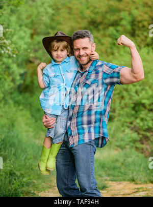 Forte il padre e il figlio nel cappello da cowboy sul ranch. kid in stivali di gomma. uomo felice papà nella foresta. natura e uomo. il giorno della famiglia. felice giornata della terra. Eco farm. piccolo ragazzo aiutare il padre in agricoltura. forti legami. Foto Stock