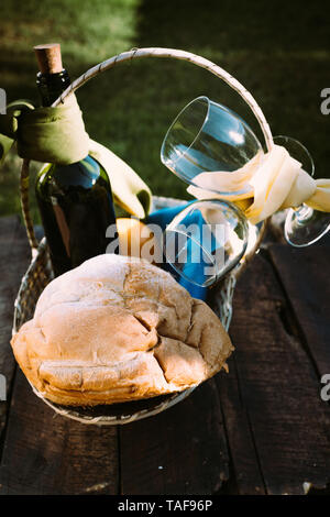 Pane casereccio, bottiglia di vino e due bicchieri in un cesto su una tavola in legno rustico Foto Stock