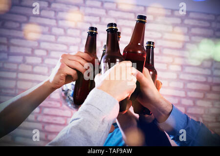 Close-up di un amico con le mani in mano la tostatura le bottiglie di birra presso il Bar contro un muro di mattoni Foto Stock