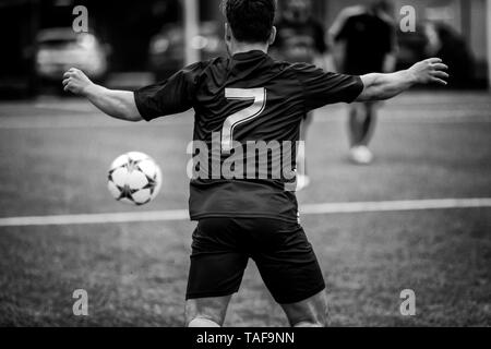 Roma, Italia - 19 Maggio 2019: giocatore di calcio in un campo di calcio insegue la palla in un gioco d'azione. Un Uomo in camicia nera e pantaloncini, incorniciato da dietro in Foto Stock