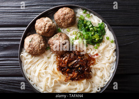 Bakso è polpetta indonesiano servito con tagliatelle, servito con le cipolle caramellate e erbe close-up su una piastra sul tavolo. Parte superiore orizzontale vista dal Foto Stock