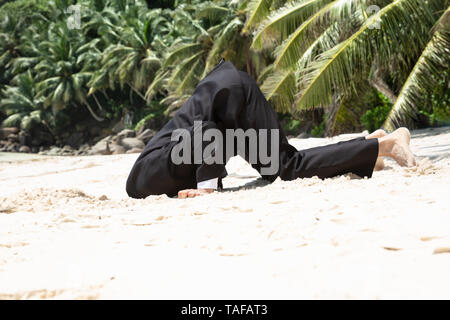 Vista laterale del soccombente imprenditore seppellendo la testa sotto la sabbia in spiaggia Foto Stock