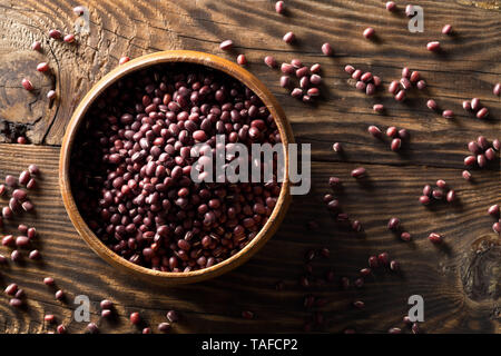 Materie, non cotte, essiccato adzuki (rosso) Mung bean in ciotola di legno su tavola in legno rustico sfondo vista superiore piatta da laici al di sopra Foto Stock