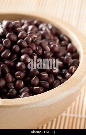 Materie, non cotte, essiccato adzuki (rosso) Mung bean in ciotola di legno su sfondo di bambù con tappetino di messa a fuoco selettiva Foto Stock