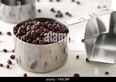 Materie, non cotte, essiccato adzuki (rosso) Mung bean in metallo tazze di misura su legno bianco sullo sfondo della tabella con il fuoco selettivo Foto Stock