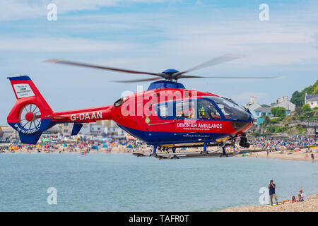 Lyme Regis, Dorset, Regno Unito. 25 maggio 2019. Devon Air Ambulance elicottero atterra sulla spiaggia affollata a Lyme Regis. L'elicottero decolla dall'affollata spiaggia con un paziente a bordo. Credito: Celia McMahon/Alamy Live News. Foto Stock