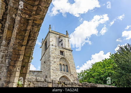 La torre del secolo XI St Olave in chiesa in York. Un arco è in primo piano e un albero è un lato. Un cielo blu con nuvole è sopra. Foto Stock