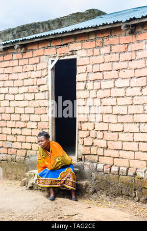 La donna si siede sui gradini all'ingresso di un villaggio chiesa del Malawi Foto Stock