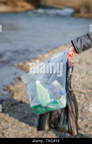 Garbage in natura, la pulizia dell'ambiente in primavera sul fiume dalle macerie di una donna in lattice monouso guanti blu nel grande blu Foto Stock