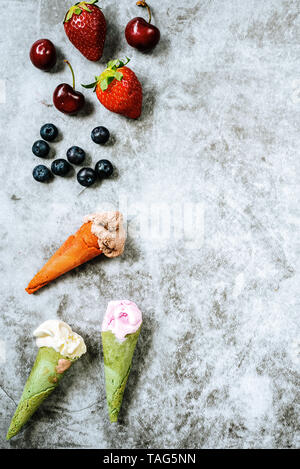 I frutti rossi come fragole ciliegie e mirtilli accanto a tre di gelati in cono su pietra chiara sfondo con copia spazio per il testo. Foto Stock