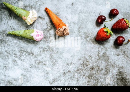 I frutti rossi come fragole ciliegie e mirtilli accanto a tre di gelati in cono su pietra chiara sfondo con copia spazio per il testo. Foto Stock