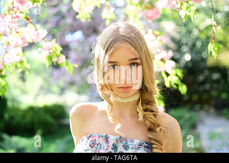 Calma ragazza bionda godendo la primavera nel giardino floreale riempito con profumi freschi di fiori di fioritura. Bella ragazza con gli occhi blu si nasconde in ombra di bl Foto Stock