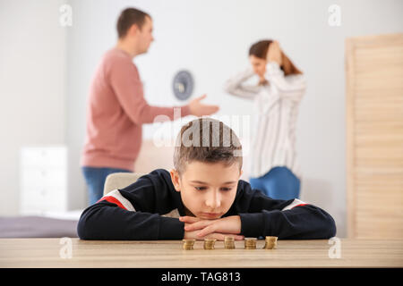 Triste ragazzino con monete e il suo quarreling genitori a casa. Concetto di supporto per il bambino Foto Stock