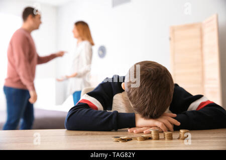 Triste ragazzino con monete e il suo quarreling genitori a casa. Concetto di supporto per il bambino Foto Stock