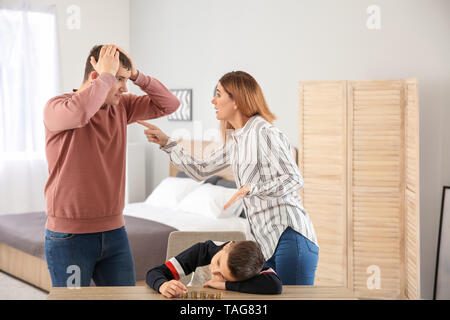 Triste ragazzino con monete e il suo quarreling genitori a casa. Concetto di supporto per il bambino Foto Stock